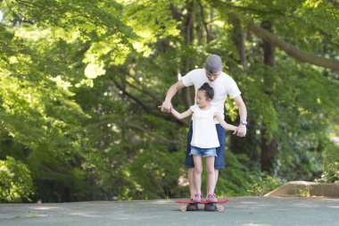 Genç baba kızına kaykay sürmeyi öğretiyor.