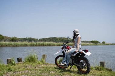 Gölün yanında motosikletli genç bir kadın. 