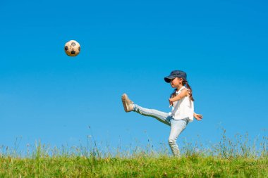 Küçük kız çimenlerde futbol oynuyor. 