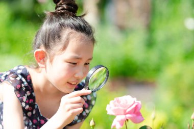 Çiçekteki büyüteçten bakan küçük kızın portresi