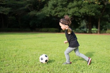 Küçük kız çimenlerde futbol oynuyor. 