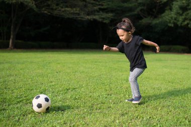 Küçük kız çimenlerde futbol oynuyor. 