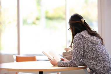 Pencerenin yanında kitap okuyan bir kadın.