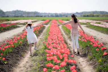 Anne ve kızı çiçek bahçesinde el ele tutuşuyorlar.