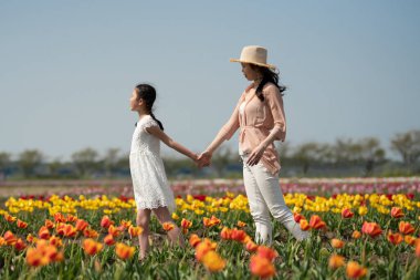 Anne ve kızı çiçek bahçesinde el ele tutuşuyorlar.