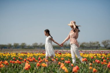 Anne ve kızı çiçek bahçesinde el ele tutuşuyorlar.
