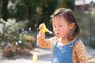 Genç Asyalı kız parkta sabun köpüğüyle oynuyor. 