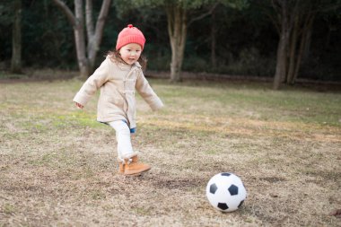 Küçük kız çimenlerde futbol topuyla oynuyor. 