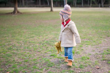 Parkta oyuncak ayıyla oynayan bir kız.