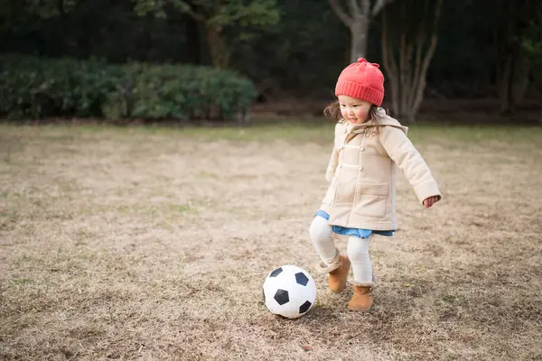 Küçük kız çimenlerde futbol oynuyor. 