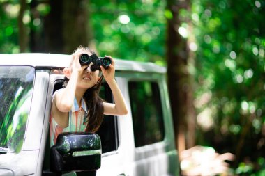 Ormanda dürbünle bakan Asyalı kız turist.