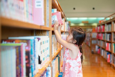 Küçük kız kütüphanede kitap seçiyor.