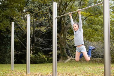 Sonbahar parkında yatay barda oynayan kız.