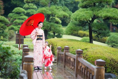 Japon bahçesinde şemsiyeli genç bir kadın ve kız.