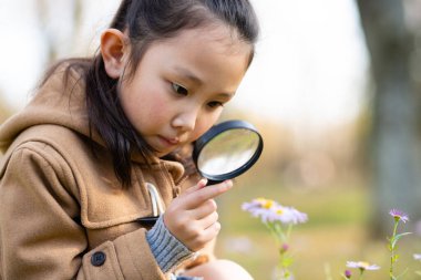 Kız elinde büyüteçle küçük bir çiçek görür.
