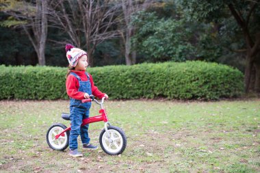Küçük sevimli Asyalı kız bahçede bisikletle oynuyor.