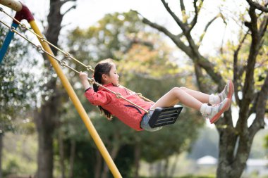 Kız bahar parkında salıncakta oynuyor.