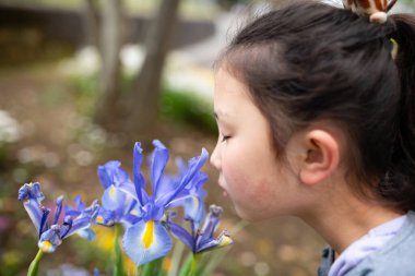 Küçük kız mavi çiçekleri kokluyor.