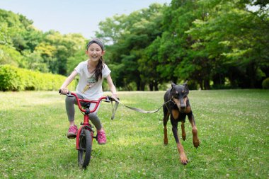 Parkta köpeğiyle bisiklet süren genç bir kız.