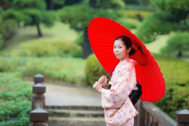 Japon bahçesinde şemsiyeli geleneksel kimono giyen Asyalı bir kız.