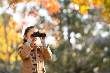 Sonbahar ormanında dürbün kullanan bir kız.