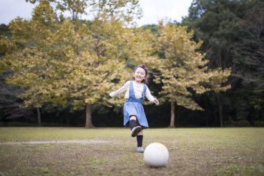 Küçük kız sonbahar parkında futbol topuyla oynuyor.