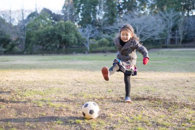 Küçük kız parkta futbol oynuyor. 
