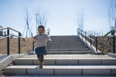 Kız parkta merdivenlerde koşuyor. 