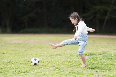 Küçük kız parkta futbol topuyla oynuyor.