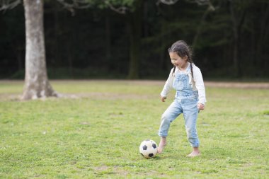 Küçük Asyalı kız yeşil çimlerde futbol topuyla oynuyor.