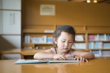 Küçük Asyalı kız kütüphanede okuyor.