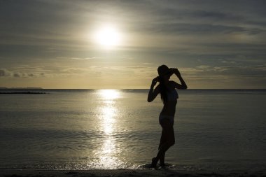Güzel bir kadının silueti gün batımında plajda dinleniyor.