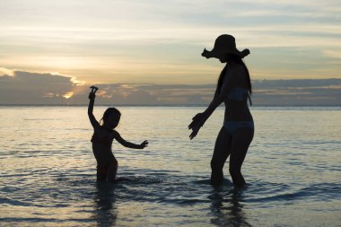 Anne ve kızı gün batımı kumsalında oynuyorlar.