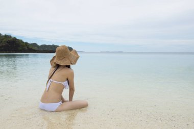 Plajda oturan mayo giymiş kadın.