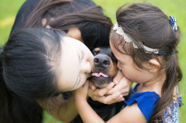 Anne ve kızı bir köpeği öpüyor.