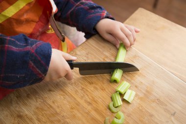 Küçük kız mutfak bıçağıyla sebze doğruyor.