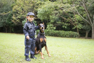 Polis kostümü giyen bir kız bir dobermanla devriyeye çıkıyor.