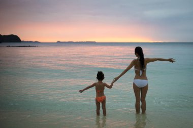 Anne ve kızı kumsalda gün batımında oynuyorlar.