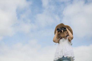 Mavi gökyüzünün arka planında dürbünü olan sevimli Asyalı bir kız.