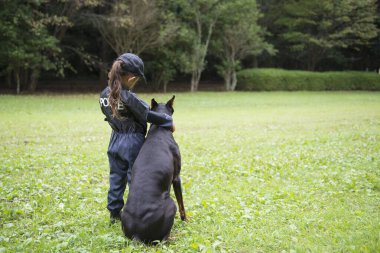 Polis kostümü giyen bir kız bir dobermanla devriyeye çıkıyor.