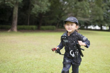 Çimlerde koşan polis kostümü giymiş bir kız.