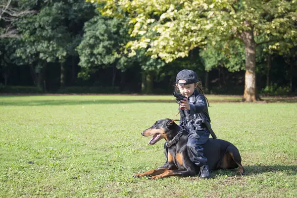 Polis kostümü giyen bir kız bir dobermanla devriyeye çıkıyor.