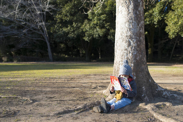 мужчина с рюкзаком сидит на земле с книгой в лесу