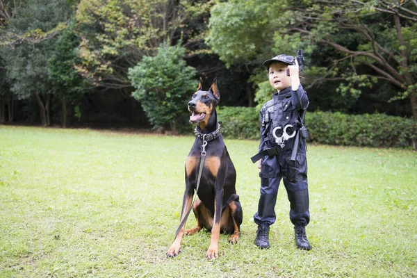 Polis kostümü giyen bir kız bir dobermanla devriyeye çıkıyor.