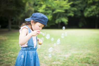 Küçük kız çayırda sabun köpüğüyle oynuyor..