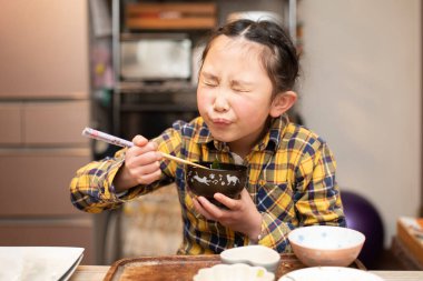Küçük kız evde çubuklarla yemek yiyor. 