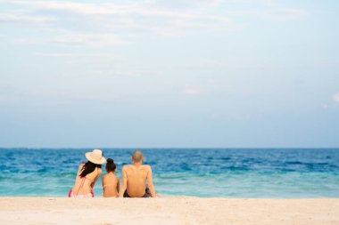 Baba, anne ve kız sahilde oturuyorlar.