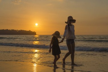 Anne ve kızı gün batımında kumsalda oynuyorlar.
