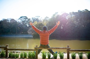 Göl kenarında elleri havada ve manzaranın tadını çıkaran bir adam.
