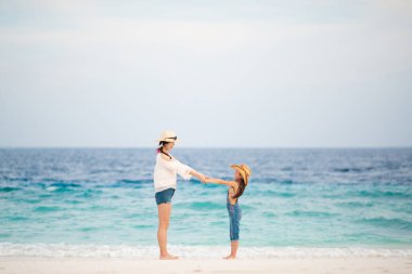 Anne ve kızı kumlu sahilde dinleniyor.